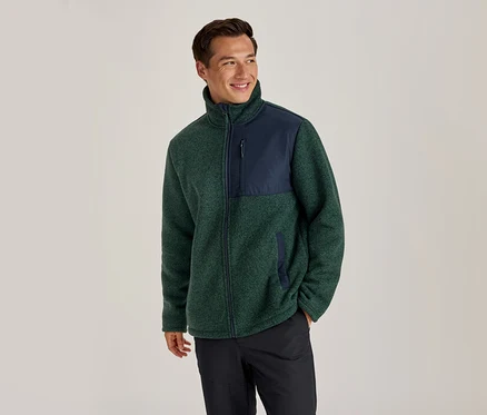 Mann trägt eine grün-marineblaue Fleecejacke und schwarze Hose, lächelt und blickt nach rechts.
