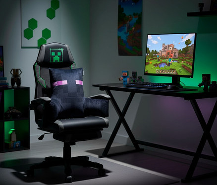 Ein Gaming-Setup mit einem schwarzen Gaming-Stuhl mit grünem Creeper-Logo und einem Enderman-Kissen. Rechts steht ein Schreibtisch mit einem Monitor, der ein Minecraft-Spiel zeigt.