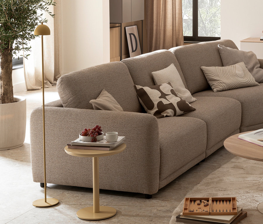 Helles, modulares Sofa mit Kissen, einer gelben SCHÖNER WOHNEN-Kollektion Akku-Stehleuchte »Bellis« und einem Beistelltisch mit Trauben und Tasse in einem Wohnzimmer.