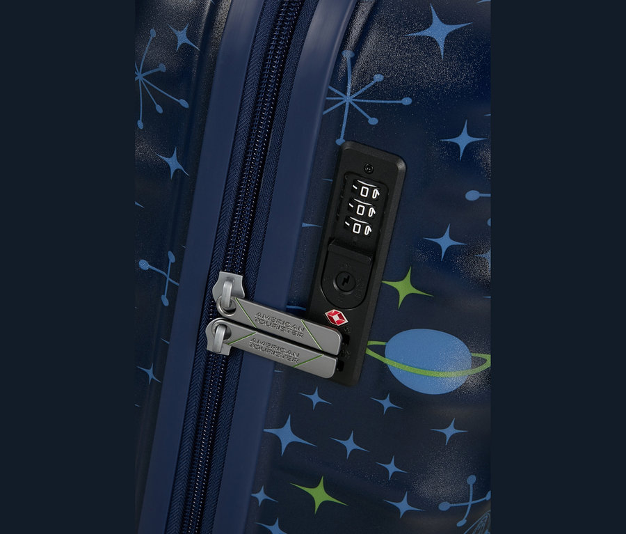 Nahaufnahme eines dunkelblauen Koffers mit Weltraum-Muster aus blauen und grünen Sternen und einem blauen Planeten. Der Koffer hat einen dunkelblauen Reißverschluss, zwei silbergraue Reißverschlusszipper mit „AMERICAN TOURISTER“-Branding und ein schwarzes Zahlenschloss mit TSA-Schlüsselloch.