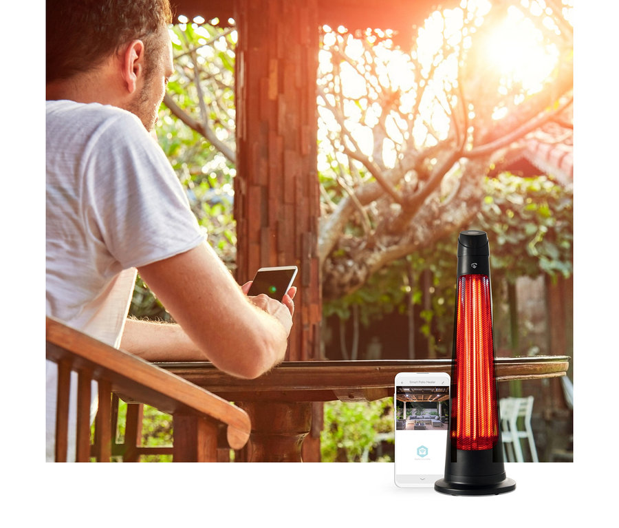 Ein Mann auf einer Holzterrasse bedient sein Smartphone, daneben ein leuchtender schwarzer Elektro-Terrassenheizer und ein weiteres Smartphone mit dessen Steuerungs-App.