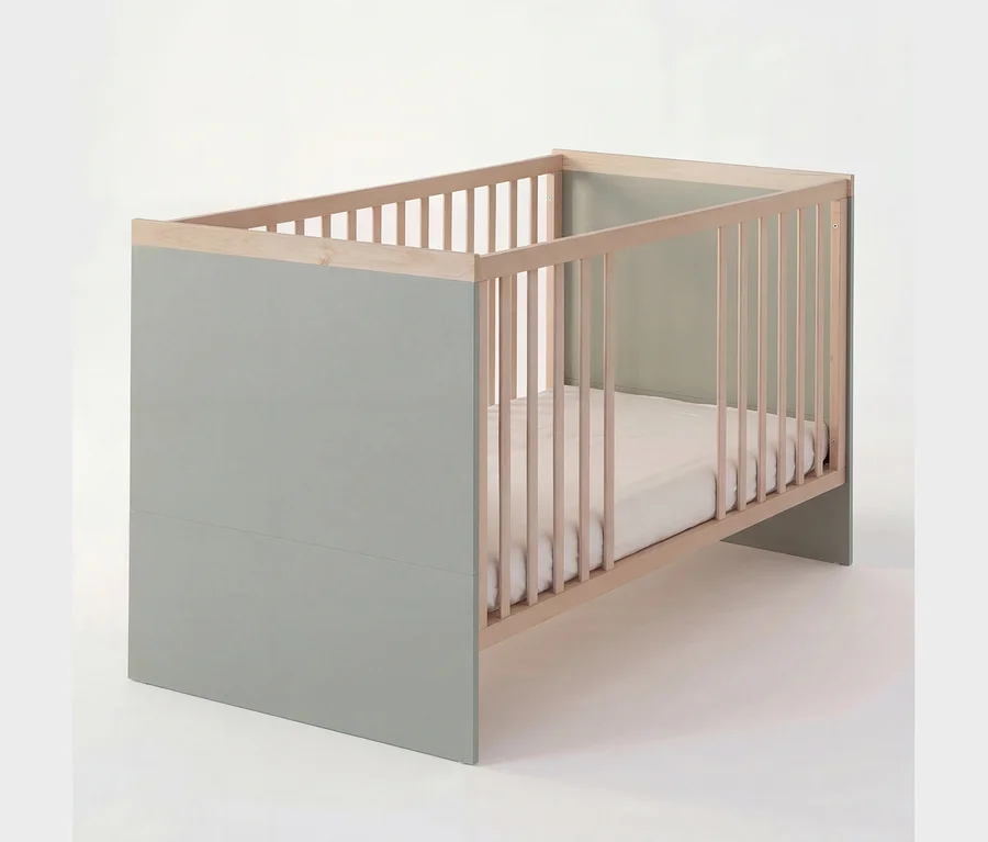 Ein Babybett in Hellgrün und Naturholz mit Gitterseiten und einer weißen Matratze.