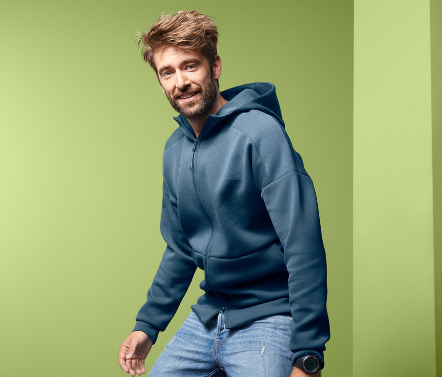 Mann posiert in blauer Funktionsjacke mit Kapuze und Jeans.