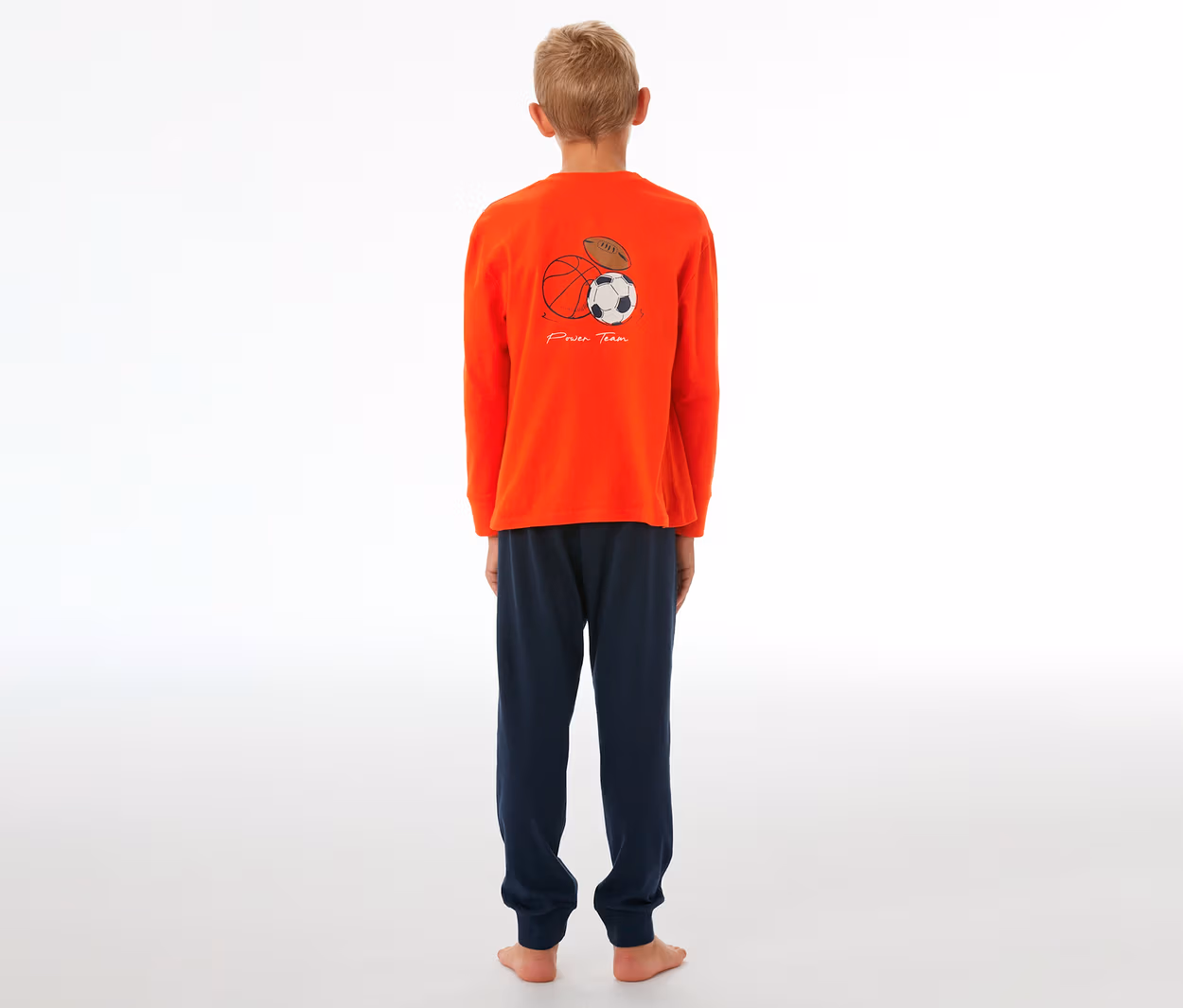 Junge in SCHIESSER Kinder-Pyjama mit Bündchen, orangefarbenes Oberteil mit Sportball-Grafik und marineblauer Hose.