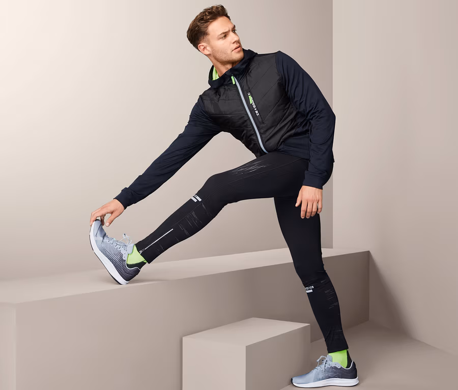 Mann dehnt Bein auf Treppe, trägt Thermo-Funktionsjacke.