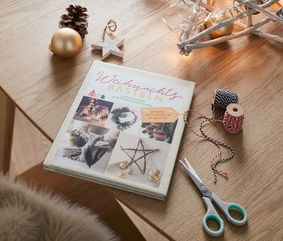 Buch »Weihnachtsbasteln« liegt auf einem Tisch neben einer Schere, Schnüren und Weihnachtsdeko.