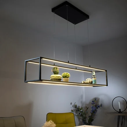 Eine schwarze LED-Pendelleuchte »Contura« hängt über einem Tisch, auf dem Dekorationen und Blumen stehen.