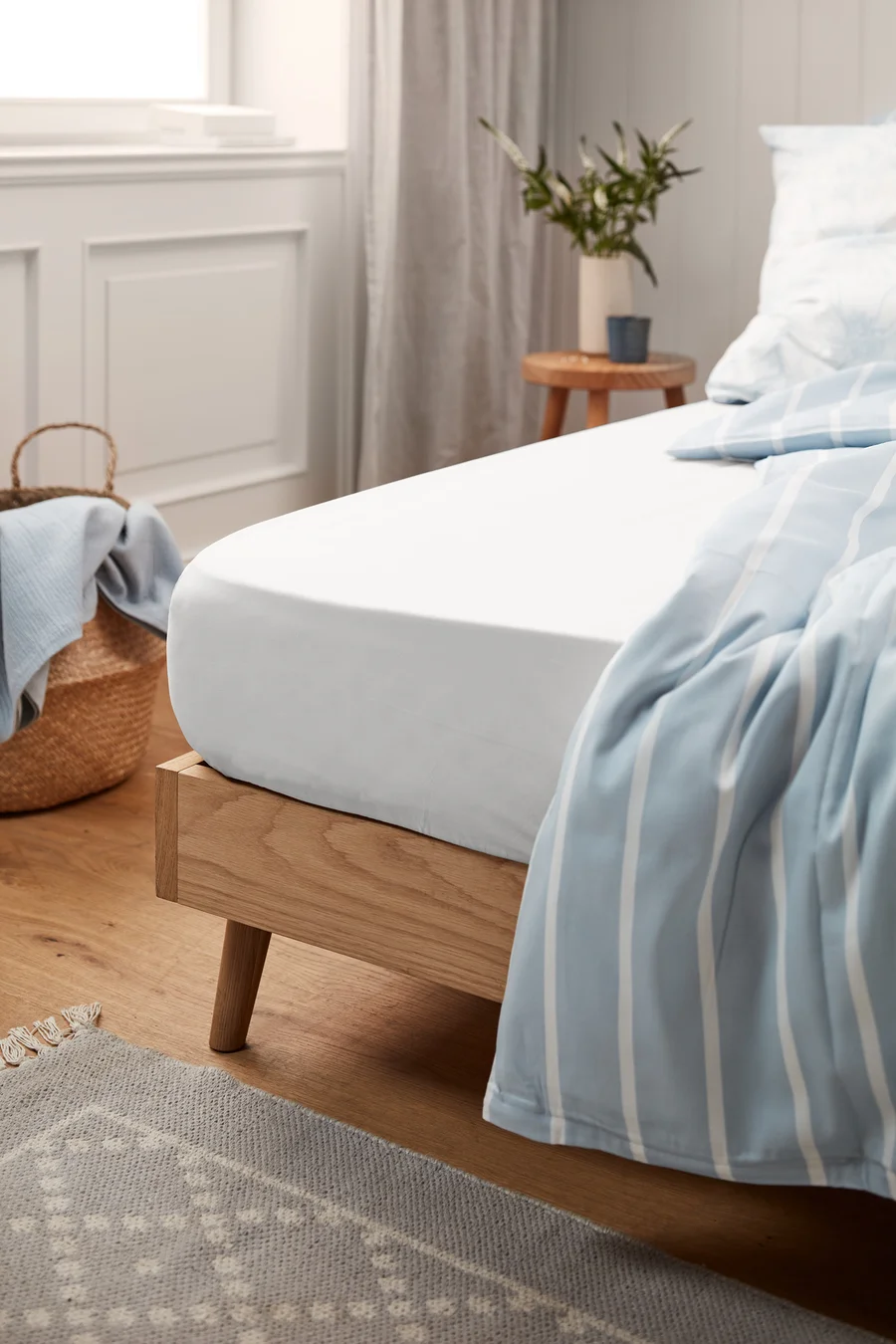 Weißes Perkal-Spannbettlaken in Standardgröße auf einem Bett mit Holzrahmen.