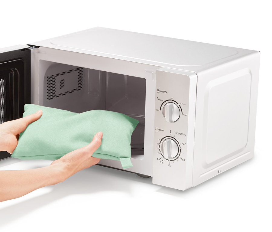 Hände legen eine Mikrowellen-Kartoffelgartasche in eine Mikrowelle.