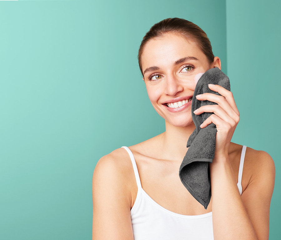 Frau reinigt ihr Gesicht mit einem grauen Microfaser-Kosmetiktuch.