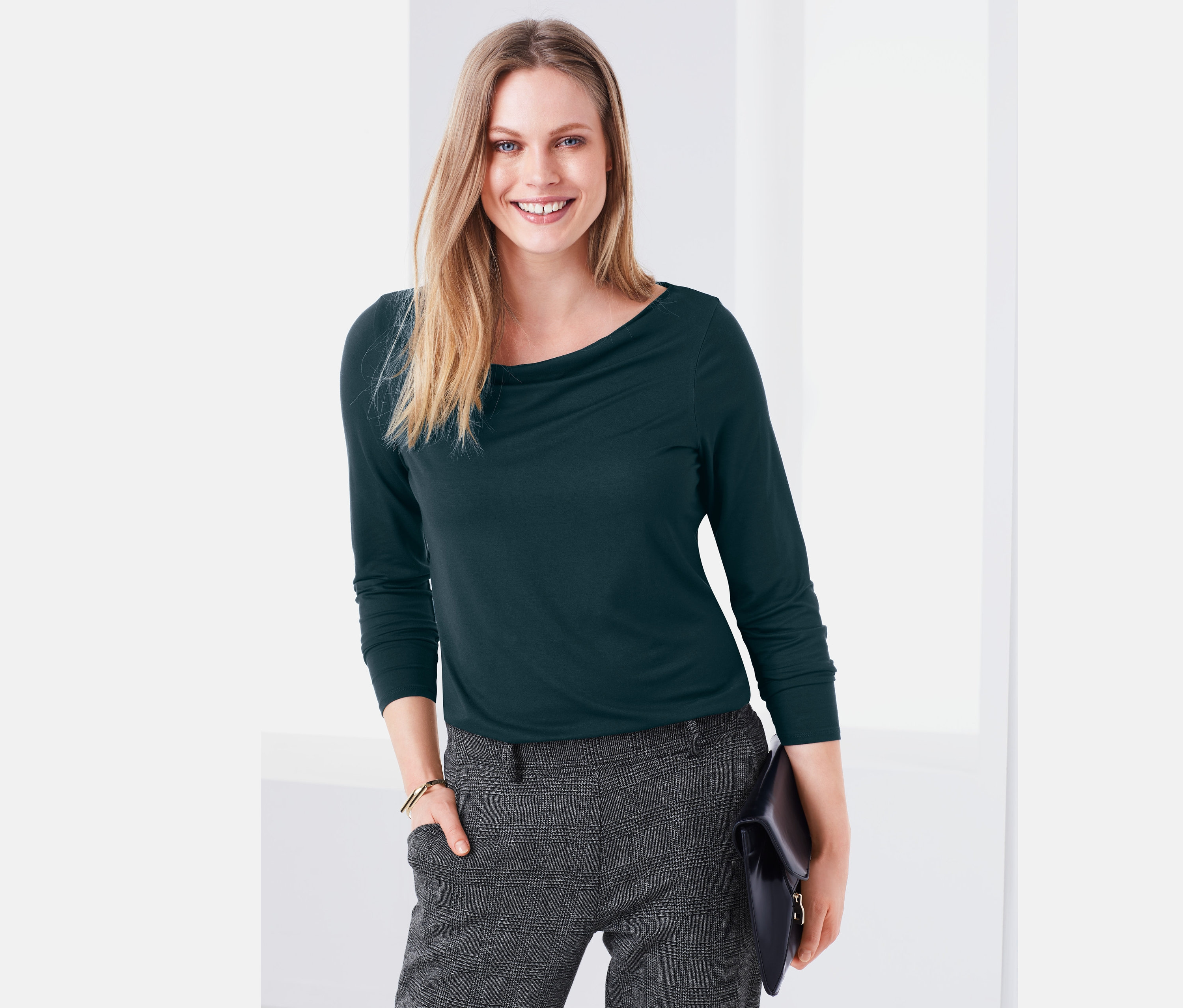 Frau trägt ein grünes Shirt mit Wasserfall-Ausschnitt und graue Hosen.