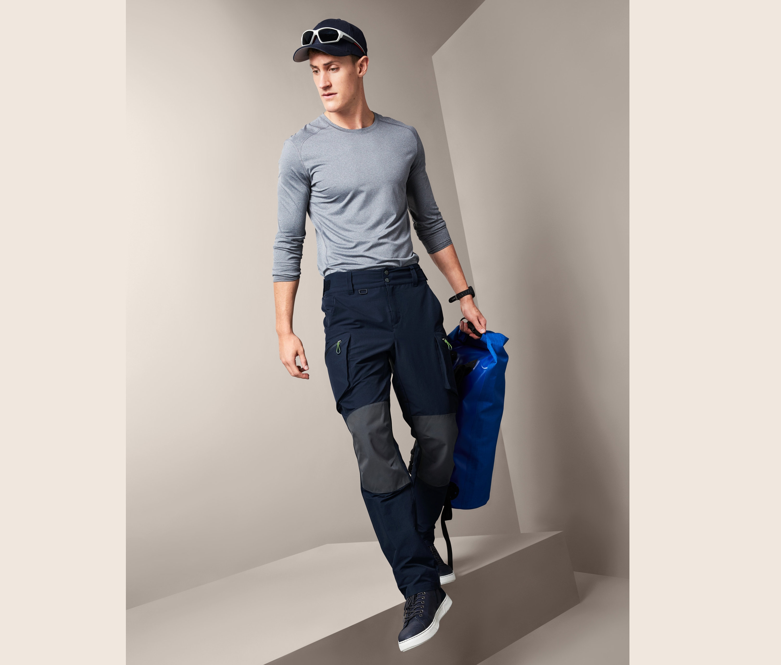Mann in grauem Shirt und dunkelblauer Segel- und Outdoorhose steigt Stufen hinab und trägt eine blaue Tasche.