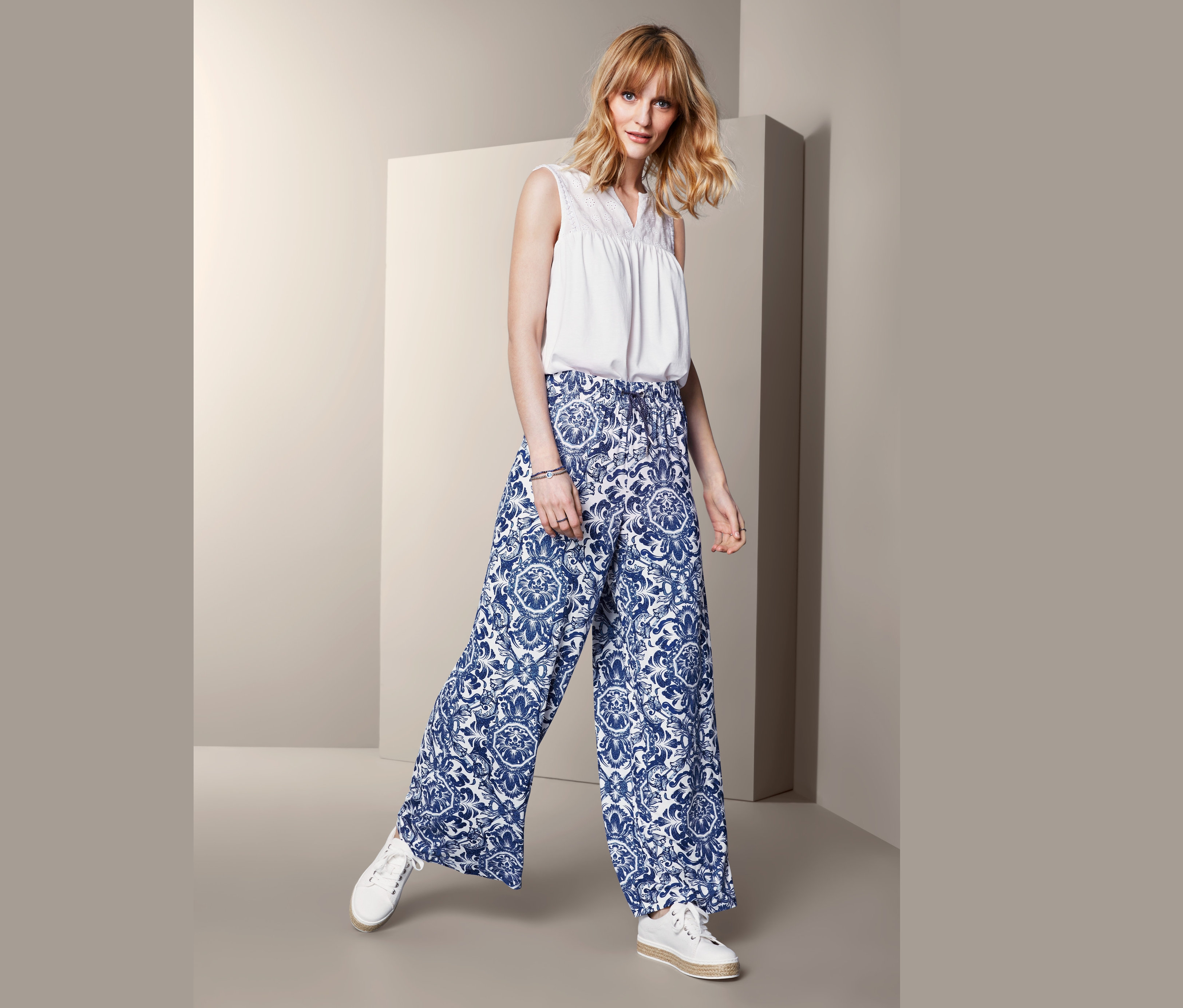 Frau posiert in bedruckter Palazzohose und weißem Oberteil.