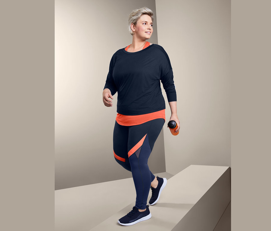 Frau geht, trägt ein 2-in-1-Sportshirt und eine Colorblocking-Sporttight.
