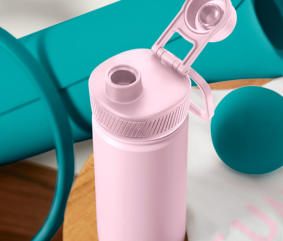Nahaufnahme einer Sport-Trinkflasche in Rosa mit offenem Deckel, daneben eine blaue Yogamatte und ein Massageball.