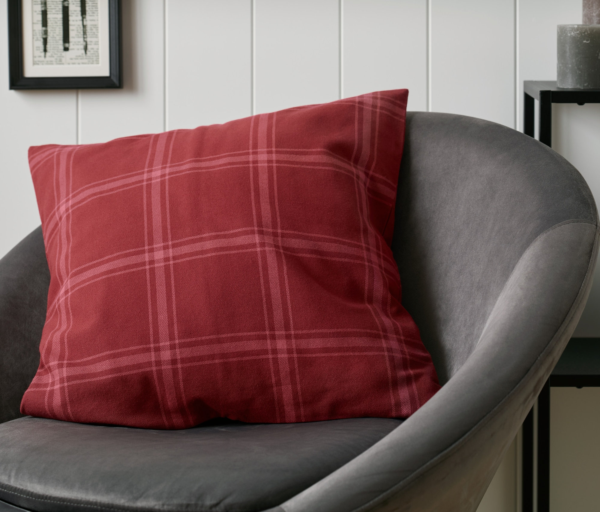 Ein rot karierter Dekokissenbezug liegt auf einem grauen Sessel.