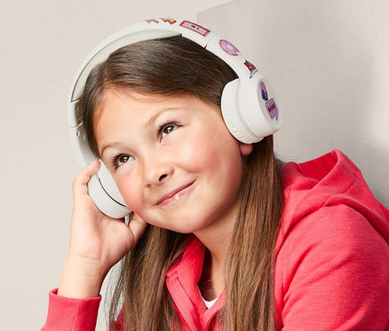 Mädchen sitzt und hört Musik mit einem kabellosen Bluetooth-Kopfhörer für Kinder.