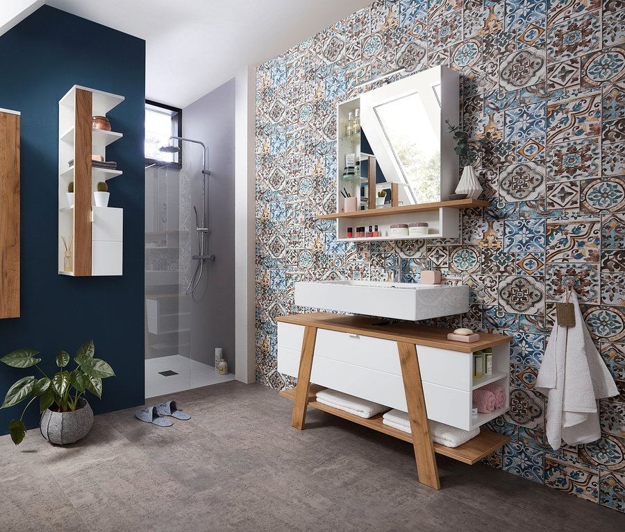 Badezimmer mit Novolino Waschbecken-Unterschrank und Novolino Spiegelschrank vor blau gemusterter Wand.