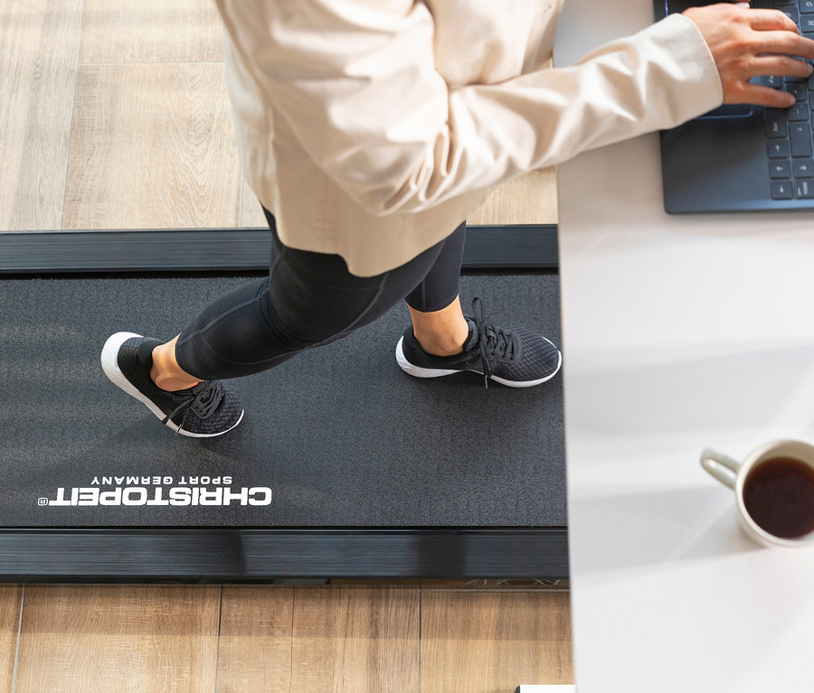 Person trainiert auf dem Christopeit Sport Walking Pad 4.0 und tippt auf einem Laptop. Auf dem Tisch stehen eine Tasse und eine Vase.