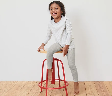 Ein Mädchen sitzt auf einem roten Barhocker und trägt graue Leggings und ein gestreiftes Langarmshirt.