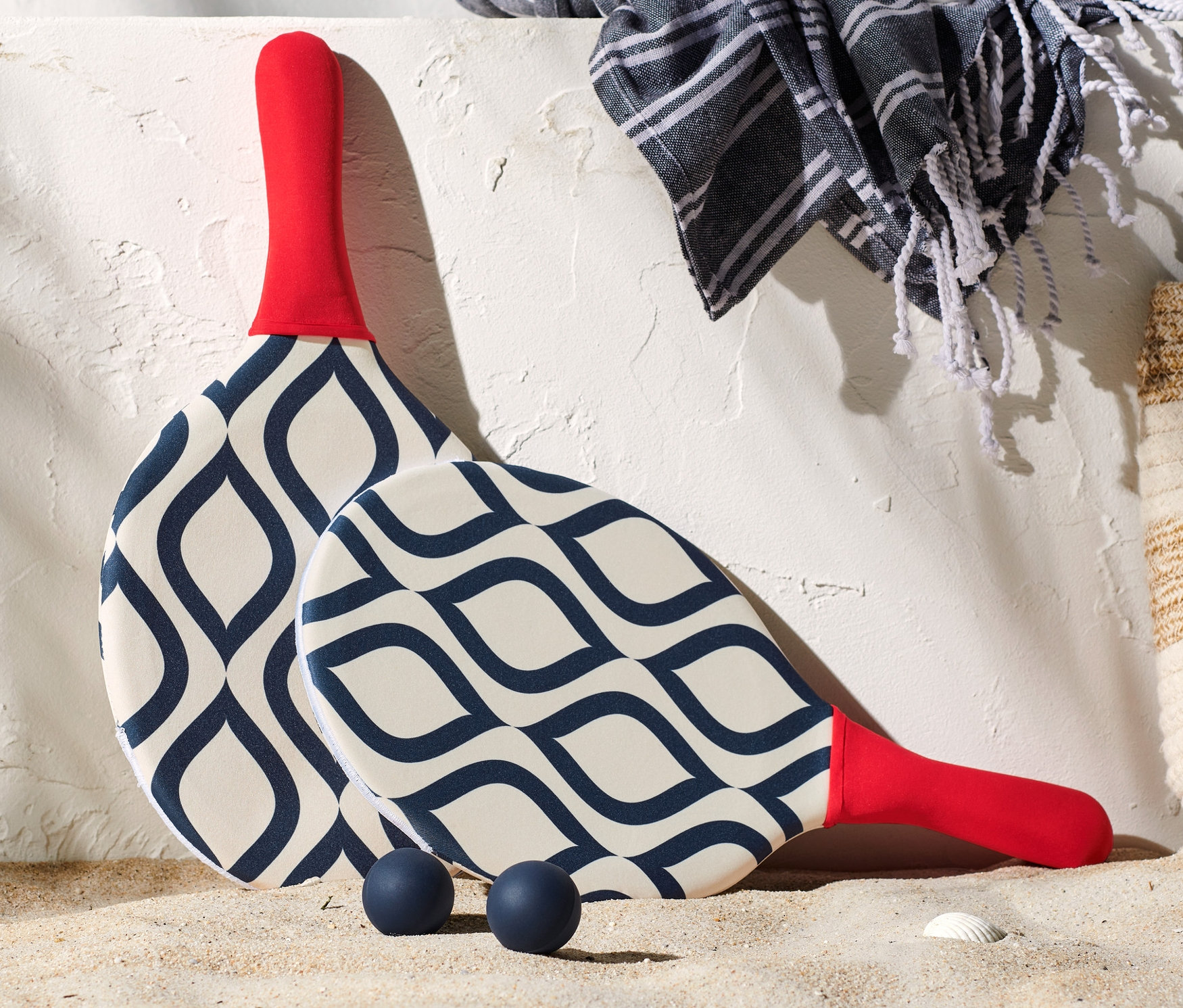 Ein Beachball-Set liegt im Sand neben einer Tasche, einem Handtuch und Sonnencreme.