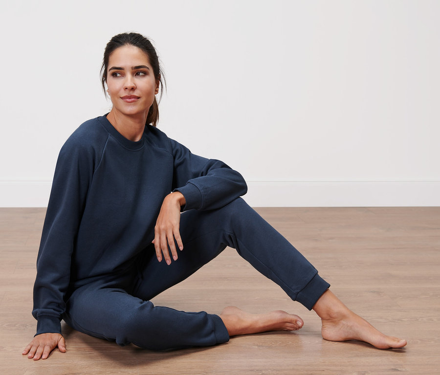 Frau sitzt in einem dunkelblauen Hausanzug auf dem Boden.