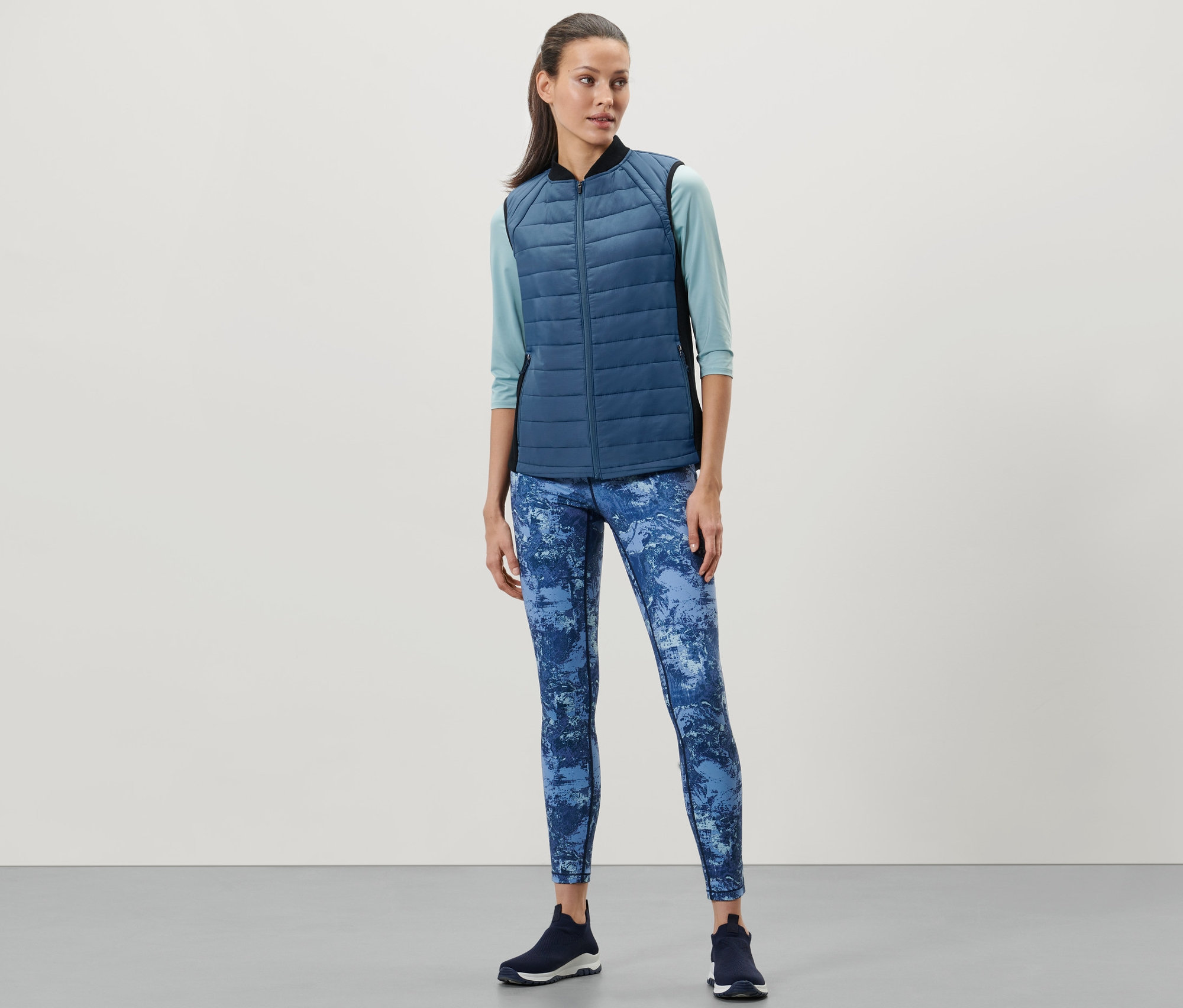 Frau trägt eine Thermo-Steppweste, blaue Leggings und dunkle Turnschuhe.