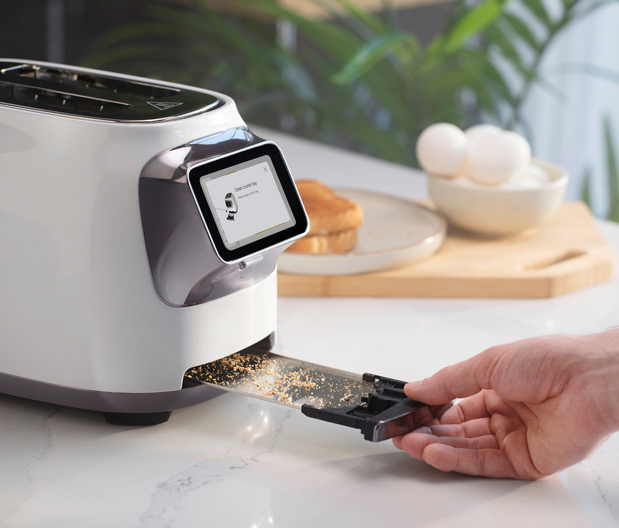 Eine Hand zieht eine Krümelschublade aus dem Tineco Toaster »Toasty One« heraus. Auf der Küchentheke liegen Brot, Eier und ein Schneidebrett.