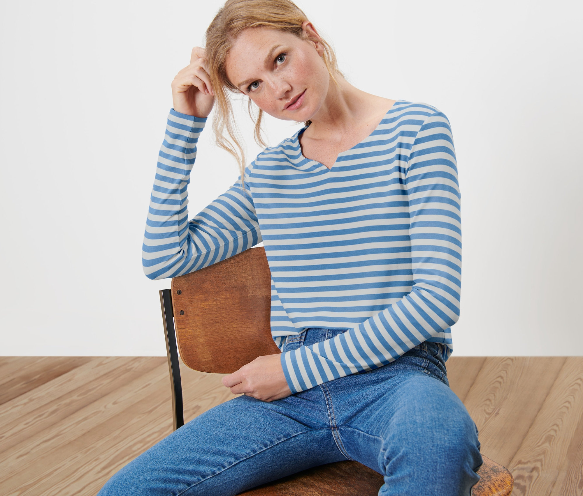 Frau sitzt auf einem Stuhl und trägt ein gestreiftes Langarmshirt.