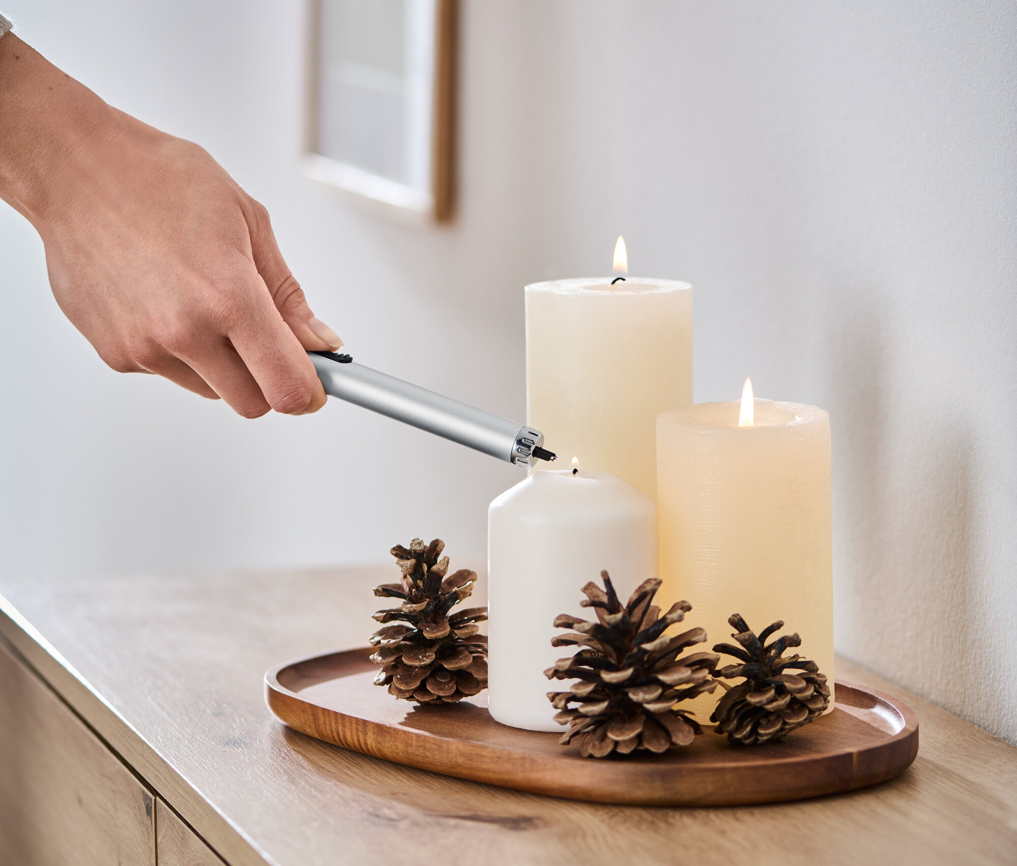 Eine Hand zündet eine weiße Kerze mit einem elektrischen Lichtbogen-Feuerzeug an.