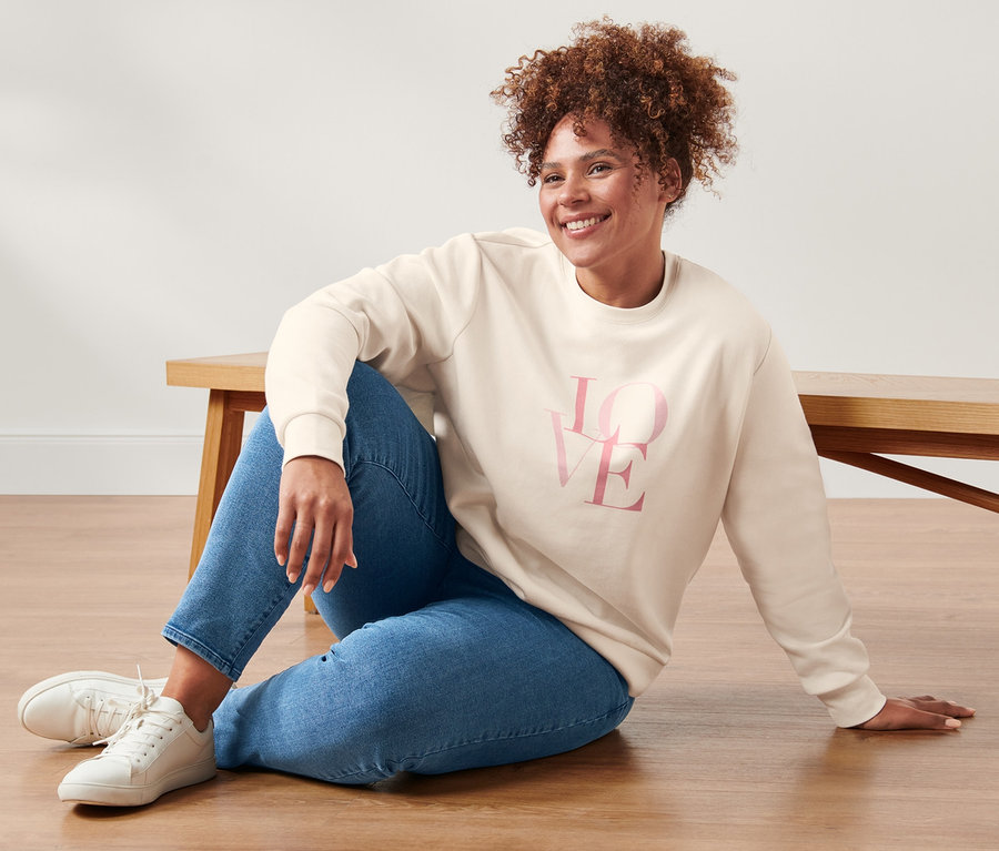 Frau sitzt in Sweatshirt und Slimfit-Jeans auf dem Boden.