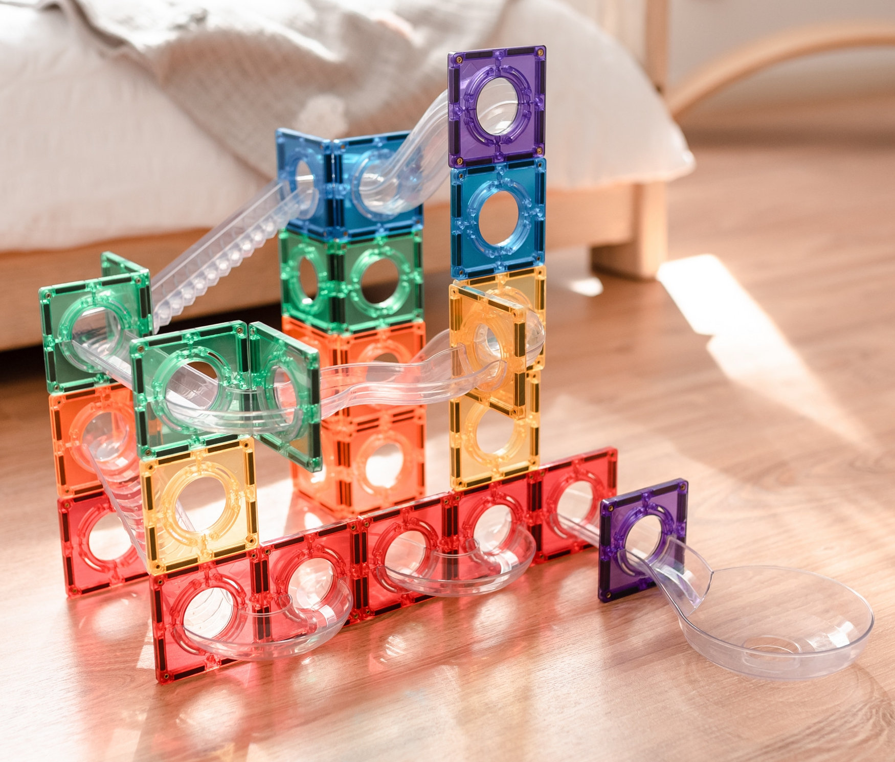 Buntes Connetix Magnetspielzeugset Kugelbahn auf Holzboden neben einem Bett.