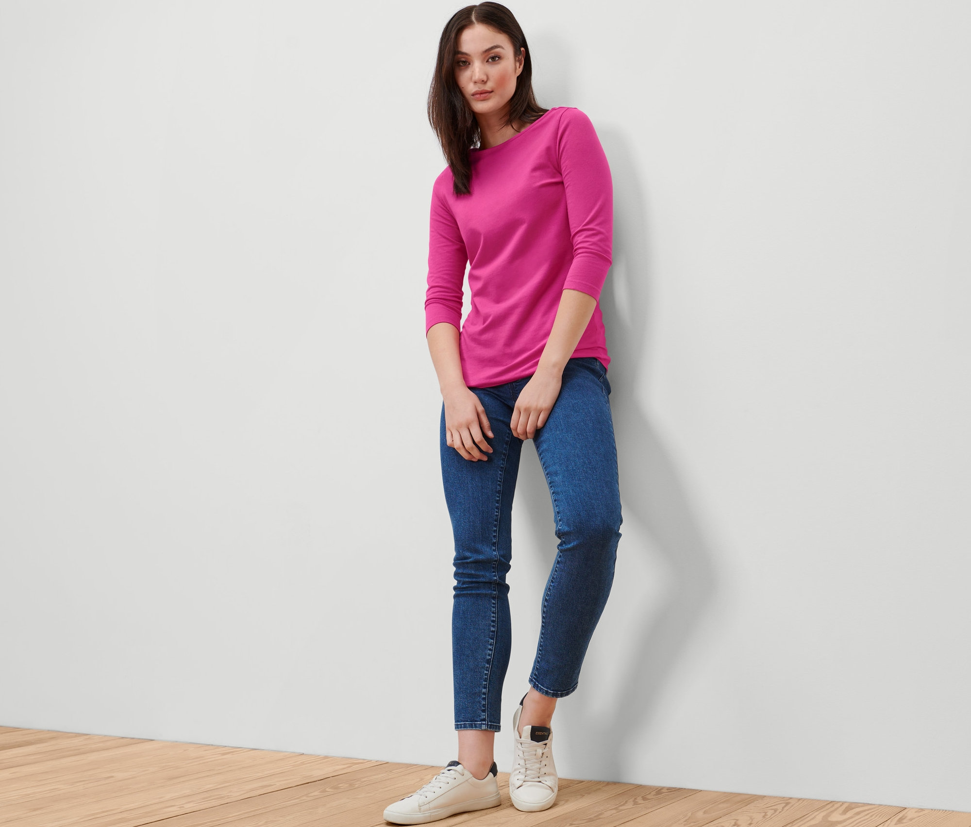 Frau posiert in einem pinkfarbenen Shirt mit 3/4-Arm und blauen Jeans.