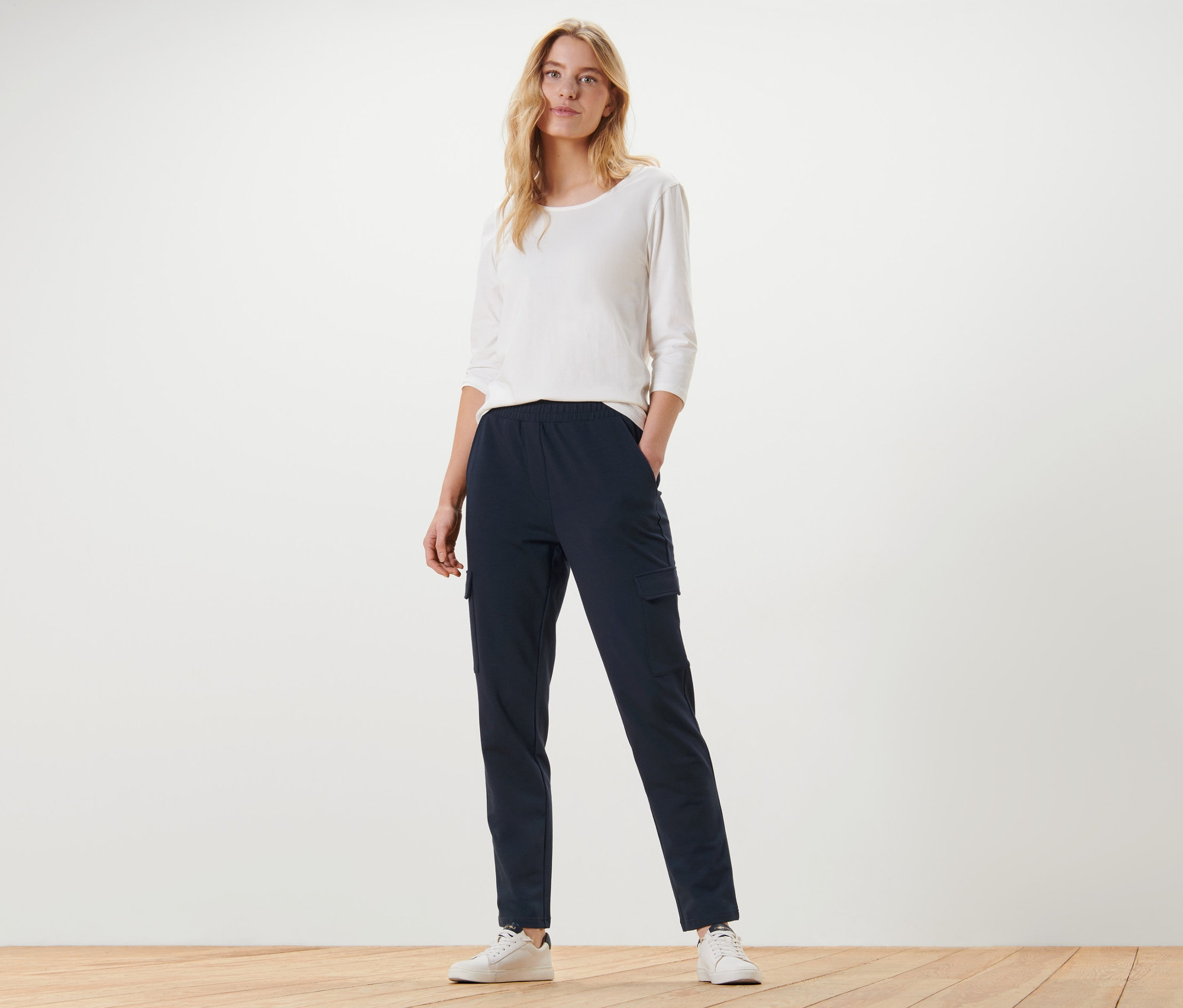 Eine Frau steht mit den Händen in den Taschen einer dunkelblauen Joggpants mit Cargo-Taschen.