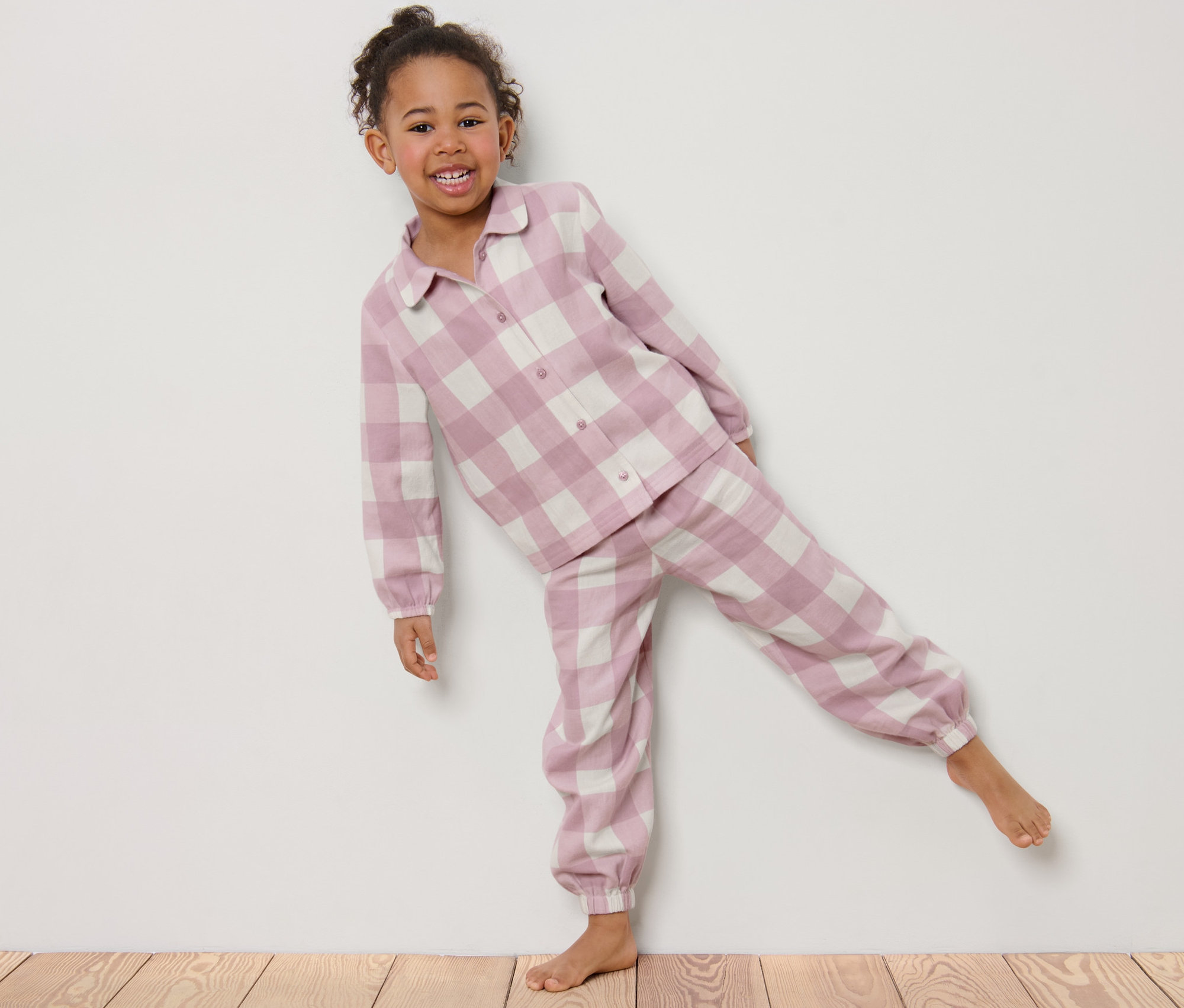 Ein lächelndes Mädchen posiert in einem Kinder-Flanell-Pyjama mit Karomuster.