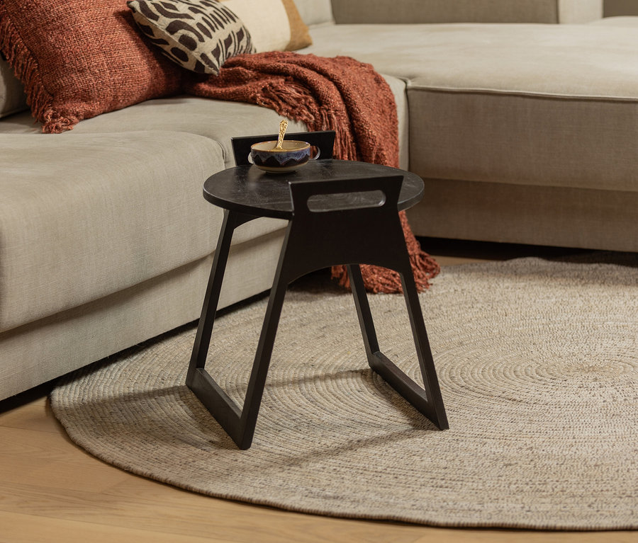 Detail eines Wohnzimmers mit beigem Sofa, braunen Kissen und einem dunklen Beistelltisch auf dem naturfarbenen Woood Teppich Utopia.