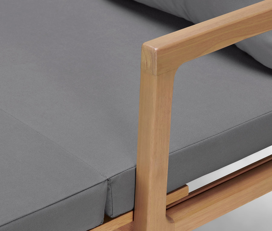 Detailaufnahme eines Loungesofas mit ausziehbarem Fußteil, grauen Kissen und hellem Holz.