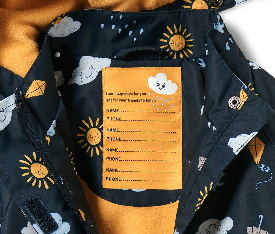 Detailaufnahme einer dunkelblauen Kleinkind-Thermo-Regenjacke mit Alloverprint von Sonne, Wolken und Drachen. Innen befindet sich ein gelbes Etikett für Name und Telefonnummer.