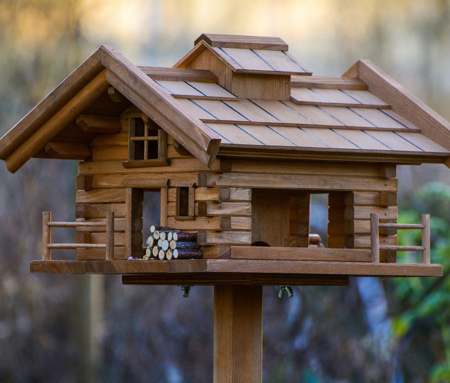 Detailansicht des Vogelfutterhauses »Tirol« aus Holz mit kleinem Holzstapel.