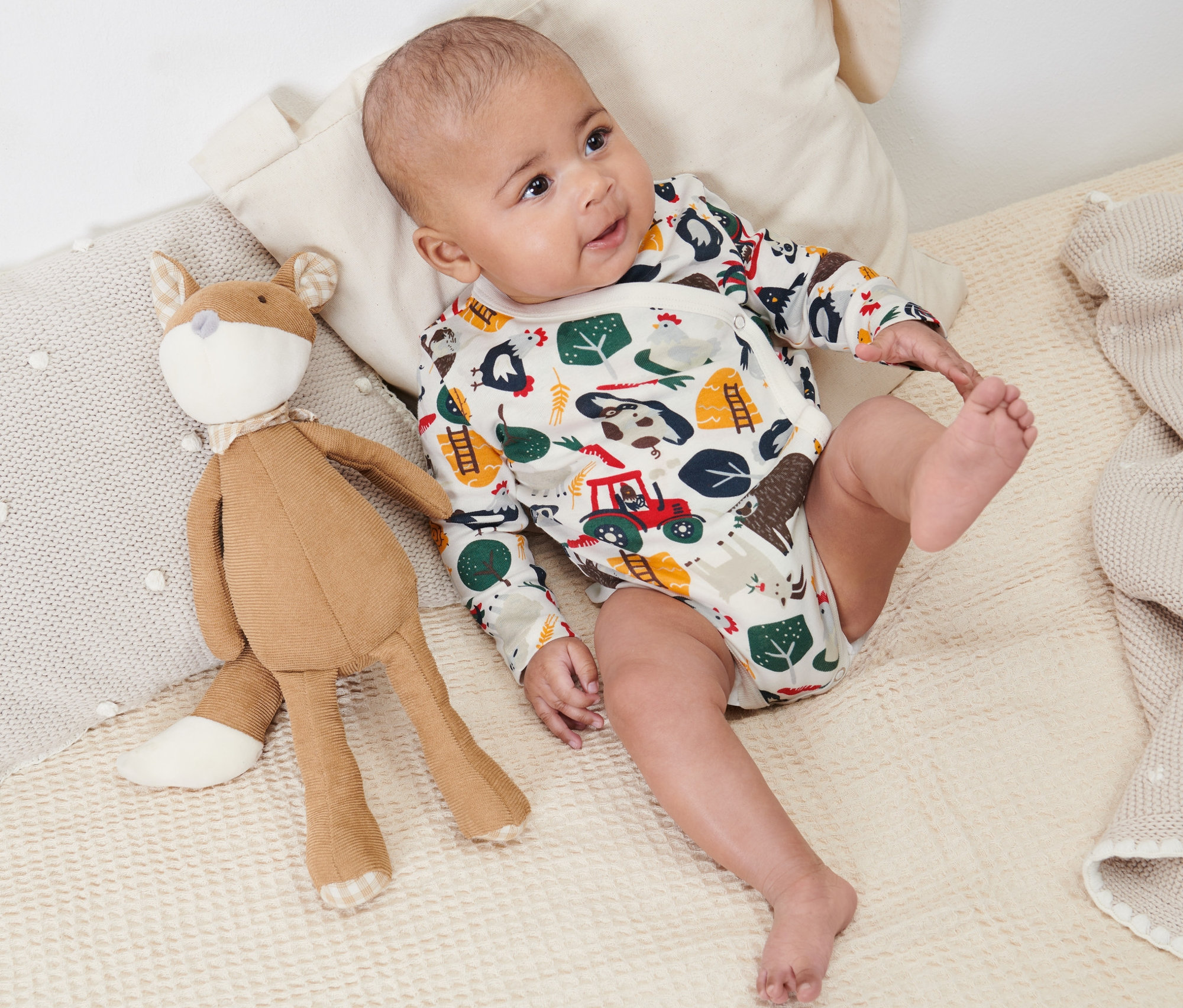 Baby liegt auf einer Decke neben einem Stofffuchs und trägt einen 2 Baby-Langarmbody.