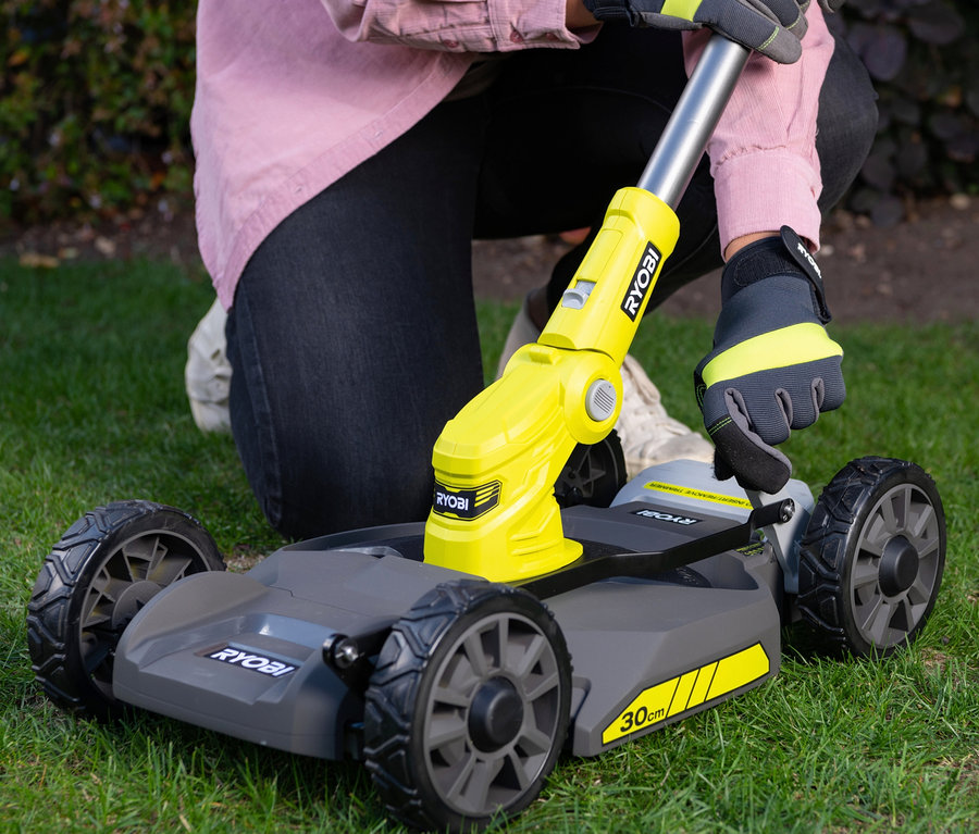 Frau kniet auf dem Rasen und benutzt einen Akku-City-Rasenmäher RYOBI 18 V One+.