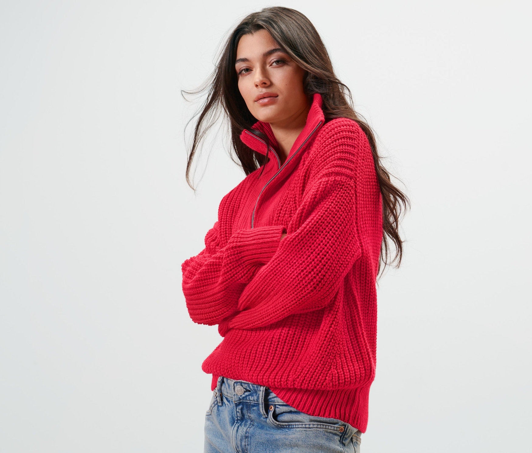 Frau trägt einen roten Grobstrick-Troyer und Jeans.