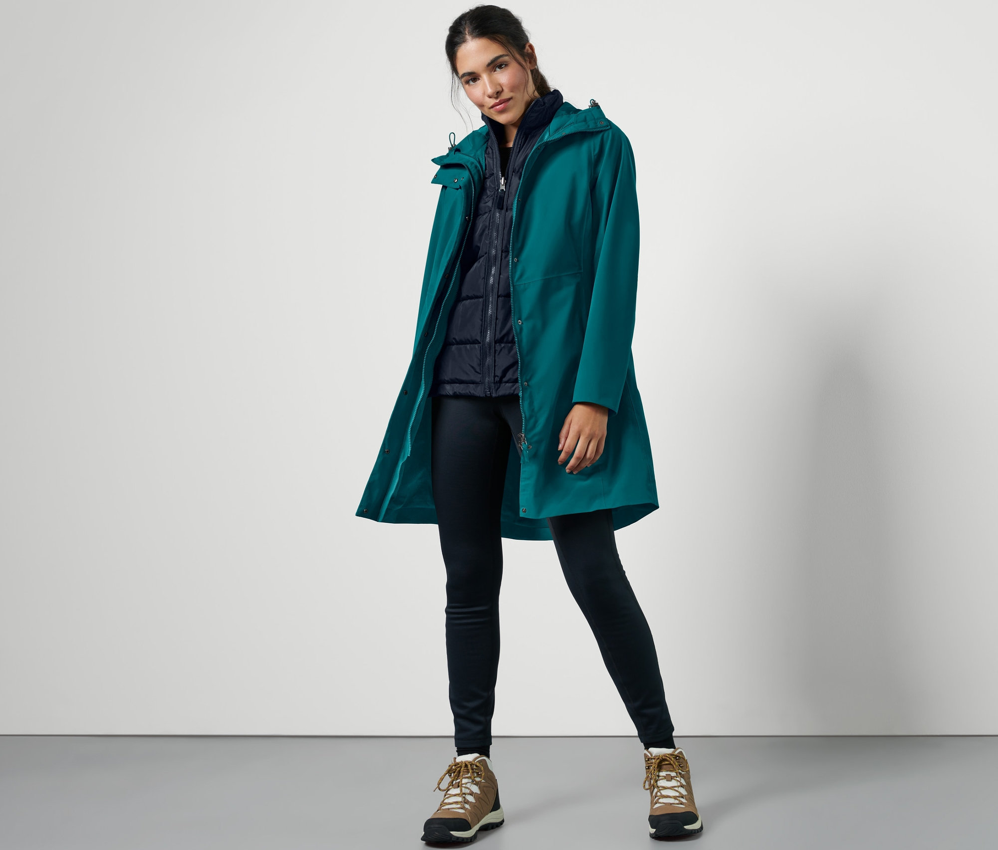 Frau posiert in einem petrolfarbenen 3-in-1-Outdoormantel mit Weste.