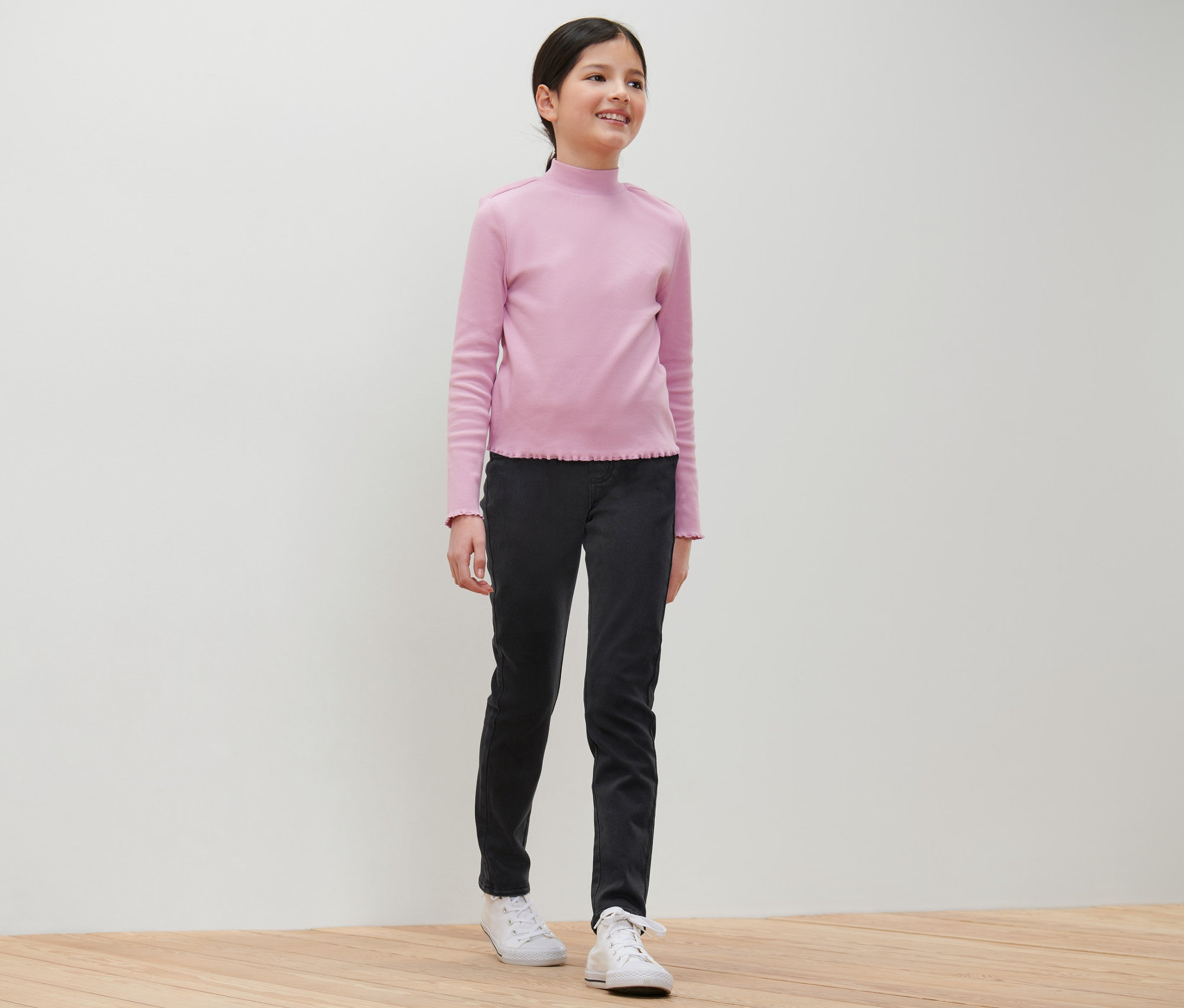 Lächelndes junges Mädchen posiert in einem hellrosa Oberteil und einer schwarzen Kinder-Treggings – Fit »Jule«.