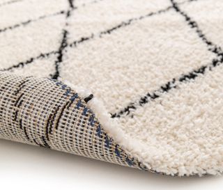 Detailansicht eines beigen Zottelteppichs mit schwarzem geometrischem Muster, Indoorteppich »NOMAD Rhombus Line«, Ø ca. 160 cm.