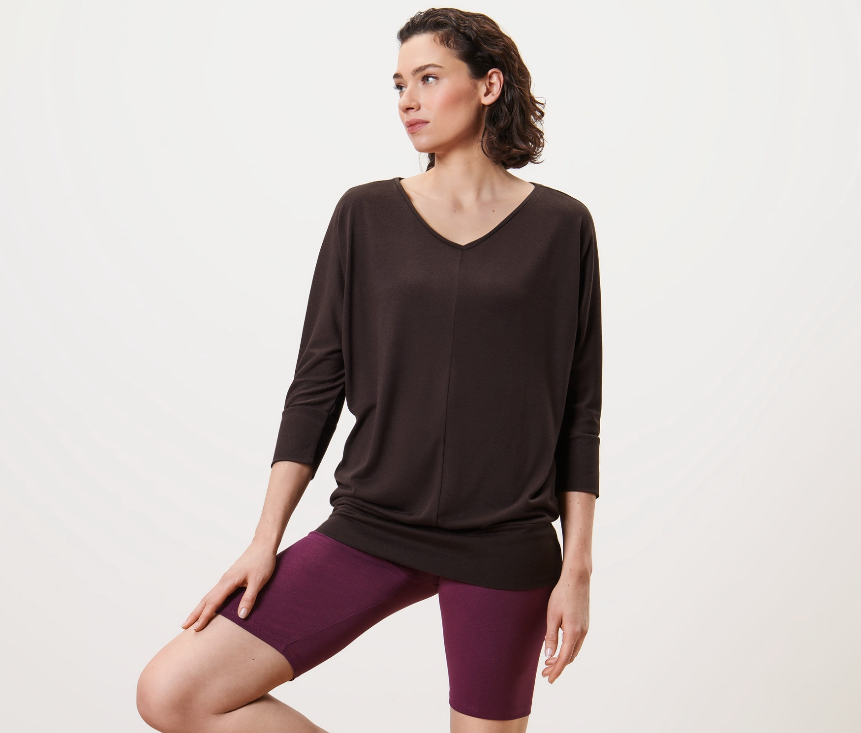 Frau posiert in Yogashirt, chocolate und violetten Shorts.