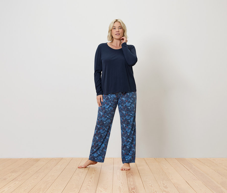 Eine Frau steht und posiert in einem marineblauen Oberteil und einer blauen Hose mit Blumenmuster.
