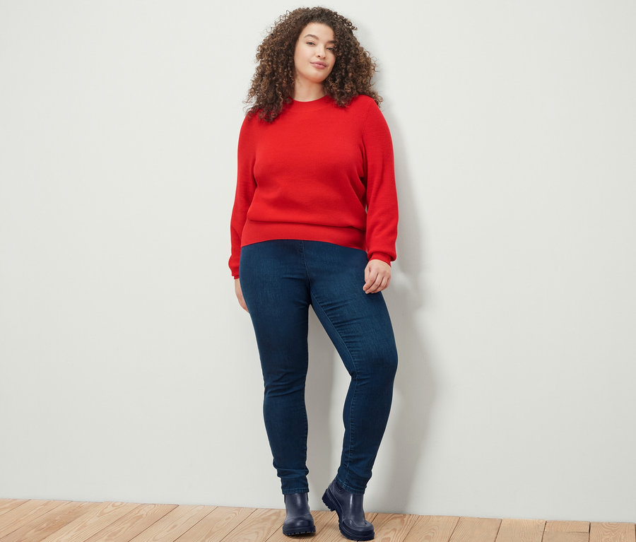 Frau posiert in rotem Feinstrickpullover und High-Waist-Denim-Leggings.