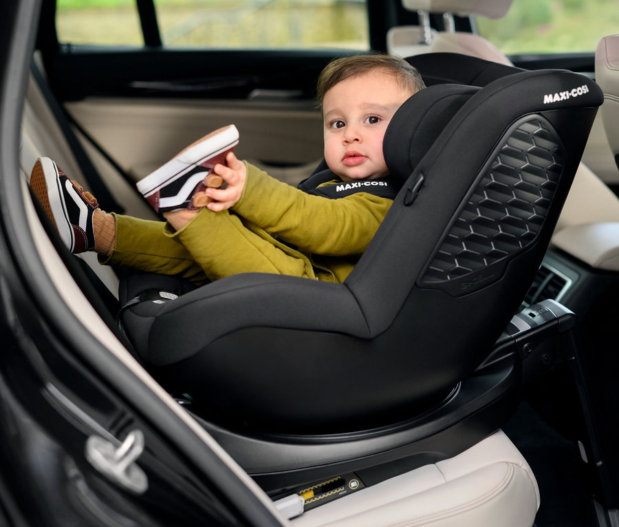 Ein Kind sitzt in einem schwarzen Maxi-Cosi Mica 360 S Kinderautositz im Auto und hält einen Schuh.