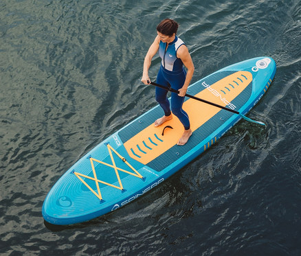 Frau steht auf Spinera SUP Board Lets Paddle 10'10" und benutzt ein Paddel.